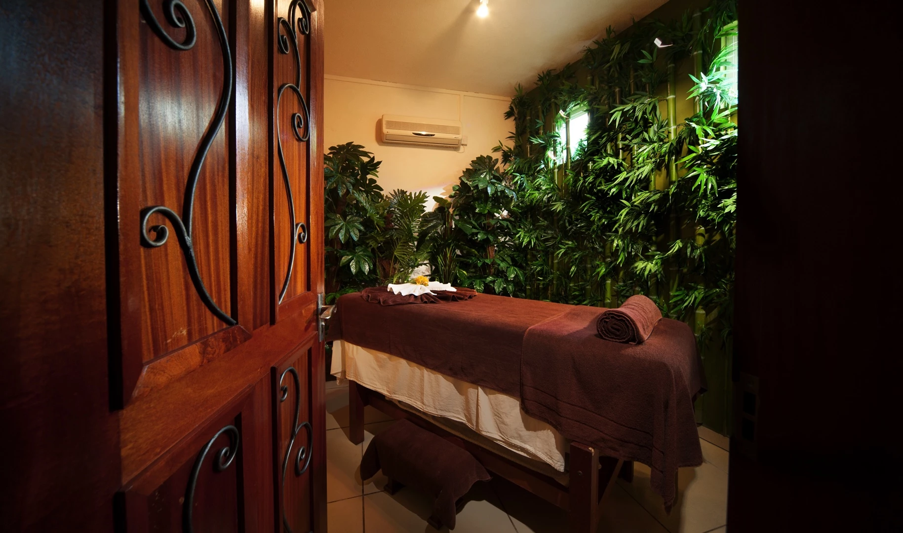 Le Palmiste spa treatment room with massage bed and tropical greenery décor.