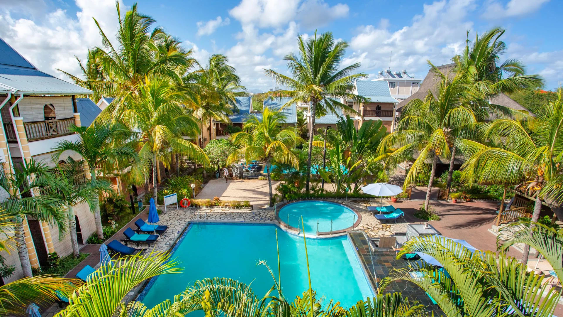 Aerial view of Le Palmiste Resort & Spa pool area surrounded by palm trees in Mauritius.